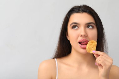 Gri arka planda patates cipsi yiyen güzel dudaklı genç bir kadın.
