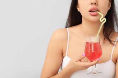 Güzel dudakları olan, gri arka planda kokteyl içen genç bir kadın.