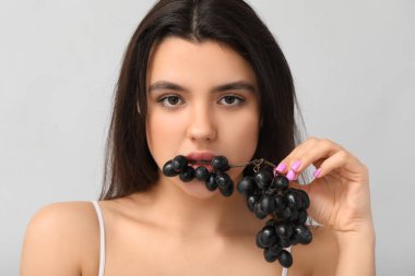 Gri arka planda olgun üzümleri olan güzel bir genç kadın, yakın plan.