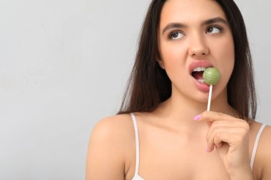 Gri arka planda lezzetli lolipop yiyen duygusal genç kadın.