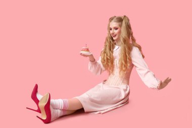 Tatlı keki olan oyuncak bebek gibi giyinmiş güzel, genç bir kadın pembe arka planda oturuyor. Sevgililer Günü kutlaması