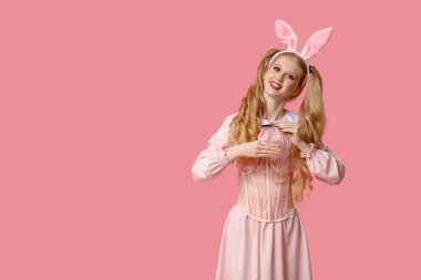 Tavşan kulaklı, pembe arka planda cüzdanı olan oyuncak bebek gibi giyinmiş güzel genç bir kadın.