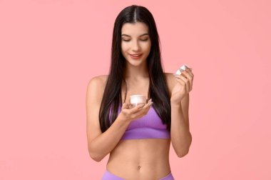 Pembe arka planda krema kavanozu olan güzel genç bir kadın.