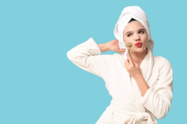 Bornozlu genç bir kadın, maske takıyor. Masaj maskesini arka planda kullanıyor.