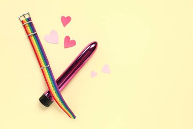 Gökkuşağı LGBT bileziği ve sarı arka planda kağıt kalpli vibratör. Sevgililer Günü kutlaması