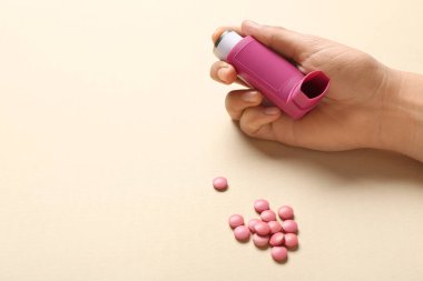 Astım spreyli çocuk eli ve bej arka planda haplar.