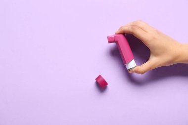 Leylak arka planında astım spreyi olan bir çocuk eli.