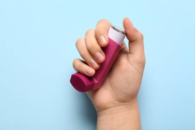 Mavi arka planda astım spreyi olan bir çocuk eli.