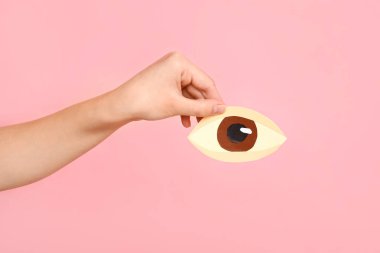 Pembe arka planda kağıt insan gözü olan kadın el, yakın plan.