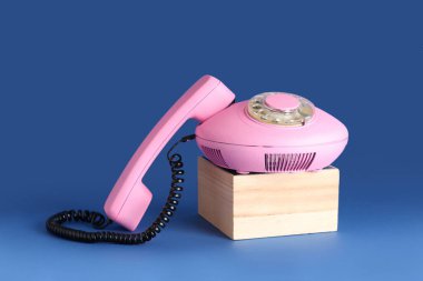 Mavi arka planda pembe retro telefonlu ahşap podyum