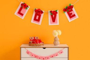 İçinde kiraz çiçekleri olan çekmeceler, hediye kutuları ve turuncu duvarın yanındaki çiçekler. Sevgililer Günü kutlaması