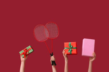 Kadın eli hediyeleri tutuyor, yoga bloğu ve bordo arka planda badminton raketleri. Noel spor kompozisyonu