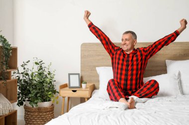 Evde yatakta kareli pijamalı yakışıklı, olgun ve mutlu bir adamın sabahı.