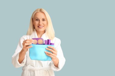 Bornoz giymiş olgun bir kadın. Elinde makyaj malzemesi olan bir çanta var.