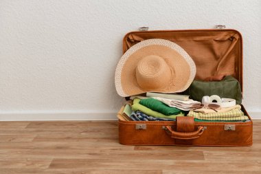 Kahverengi deri bavul. Giysiler, şapka ve gözlüklerle dolu.