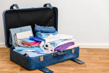 Giysiler, ayakkabılar ve kulaklıklarla dolu mavi deri bir bavul.