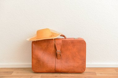Kahverengi deri bavul ve odada hasır şapka.