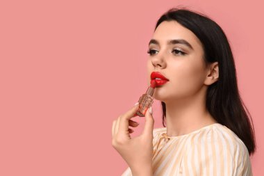 Güzel genç bir kadın pembe arka plana ruj sürüyor.