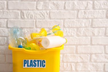 Beyaz tuğla duvarın yanında plastik olan sarı geri dönüşüm kutusu. Geri dönüşüm kavramı