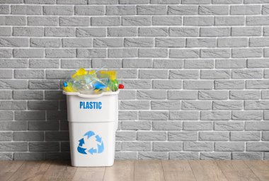 Gri tuğla duvarın yanında PLASTIC işareti olan tam çöp kutusu. Geri dönüşüm kavramı
