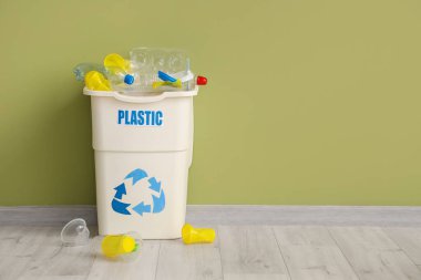 Yeşil duvarın yanında PLASTIC işareti olan tam çöp kutusu. Geri dönüşüm kavramı