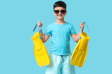 Güneş gözlüklü şirin çocuk mavi arka planda palet tutuyor.