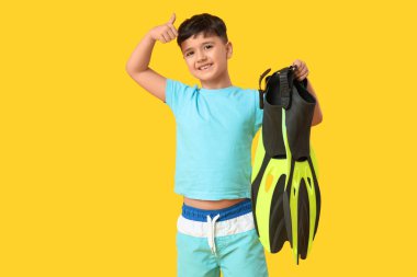 Palet tutan ve sarı arka planda baş parmağını gösteren sevimli küçük çocuk.