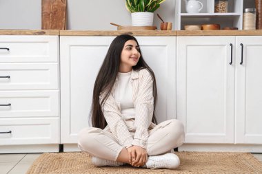 Evdeki mutfakta yerde oturan güzel, genç ve mutlu bir kadın.
