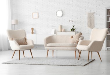 Beyaz tuğla duvara karşı kanepe ve koltuklu oturma odasının içinde.