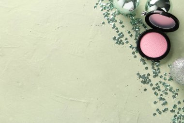 Noel topları, makyaj allığı ve yeşil arkaplanda pullarla güzel bir kompozisyon.