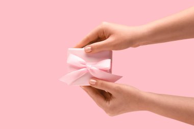 Female hands with gift box on pink background