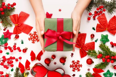 Noel hediyesi kutusu olan kadın eller, köknar ağacı dalları ve beyaz arka planda süslemeler.