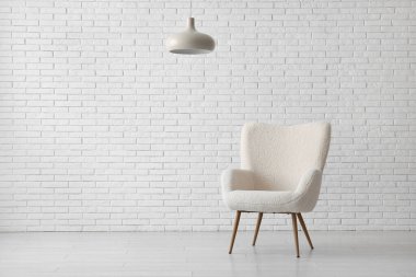 Beyaz tuğla duvarın yanında rahat koltuk ve lamba.