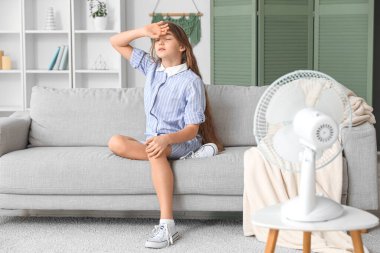 Oturma odasında elektrikli vantilatörü olan genç kız.