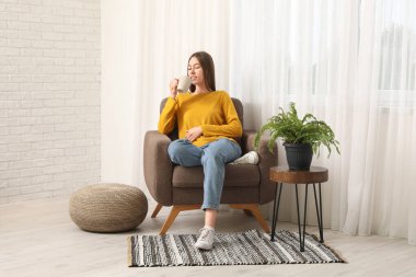 Oturma odasının penceresinin yanındaki rahat koltukta kupası olan güzel genç bir kadın.