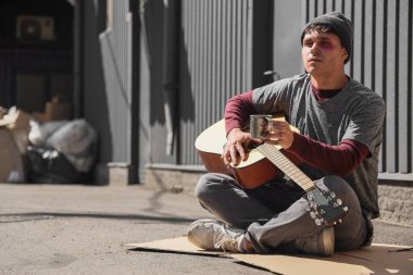 Sokaklarda gitar çalan genç evsiz bir adam.