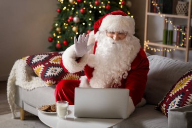 Evde kanepede dizüstü bilgisayarlı Noel Baba sohbet ediyor.