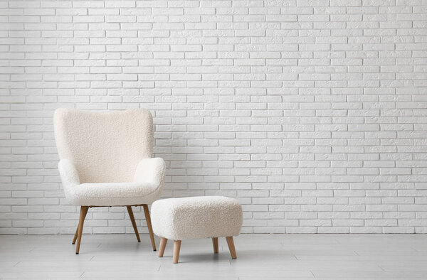 Comfortable armchair with pouf near white brick wall