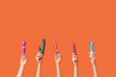 Turuncu arka planda farklı vibratörlere sahip kadın elleri.