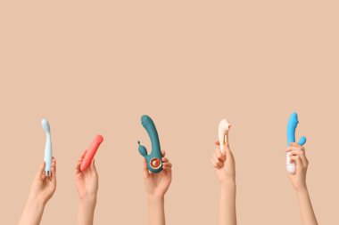 Kahverengi arka planda farklı vibratörlere sahip kadın elleri.