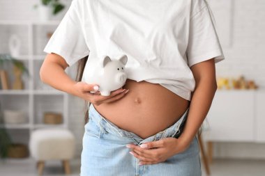 Evinde domuz kumbarası olan genç hamile bir kadın, yakın plan. Annelik Faydası konsepti