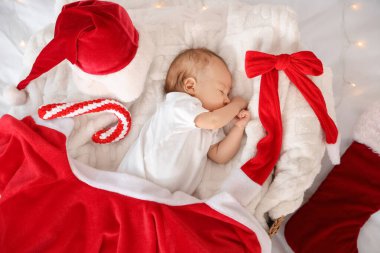 Noel dekoru olan, yatakta sepetin içinde uyuyan şirin bir bebek.