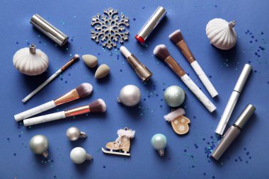 Dekoratif kozmetik ürünleri, makyaj fırçaları ve mavi arka planda Noel süslemeleri olan kompozisyon