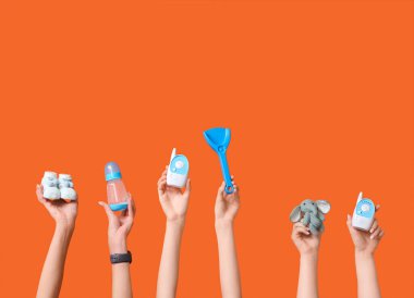 Turuncu arka planda farklı bebek aksesuarları olan kadın elleri.