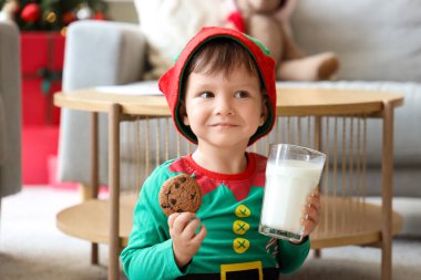 Noel arifesinde evde elinde bir bardak süt ve kurabiyeyle küçük şirin bir çocuk.