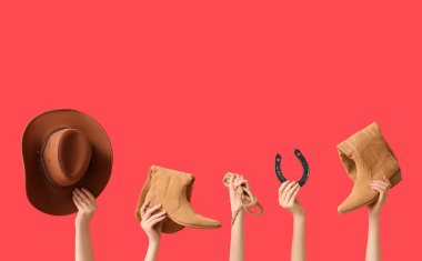 Kırmızı arka planda kovboy şapkası, ayakkabısı, kement ve at nalı olan kadın eller.