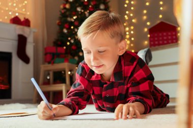 Noel arifesinde evde Noel Baba 'ya mektup yazan sevimli küçük çocuk.