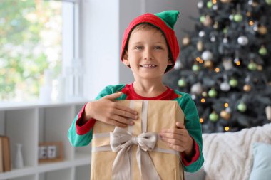 Evde hediye kutusuyla Noel elfi gibi giyinmiş şirin, mutlu bir çocuk.