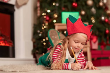 Noel arifesinde Noel Baba 'ya mektup yazan elf kostümlü şirin küçük bir kız.