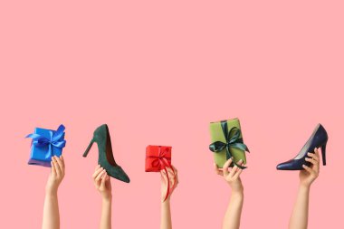 Farklı ayakkabıları ve pembe arka planda Noel hediye kutuları olan birçok kadın eli.